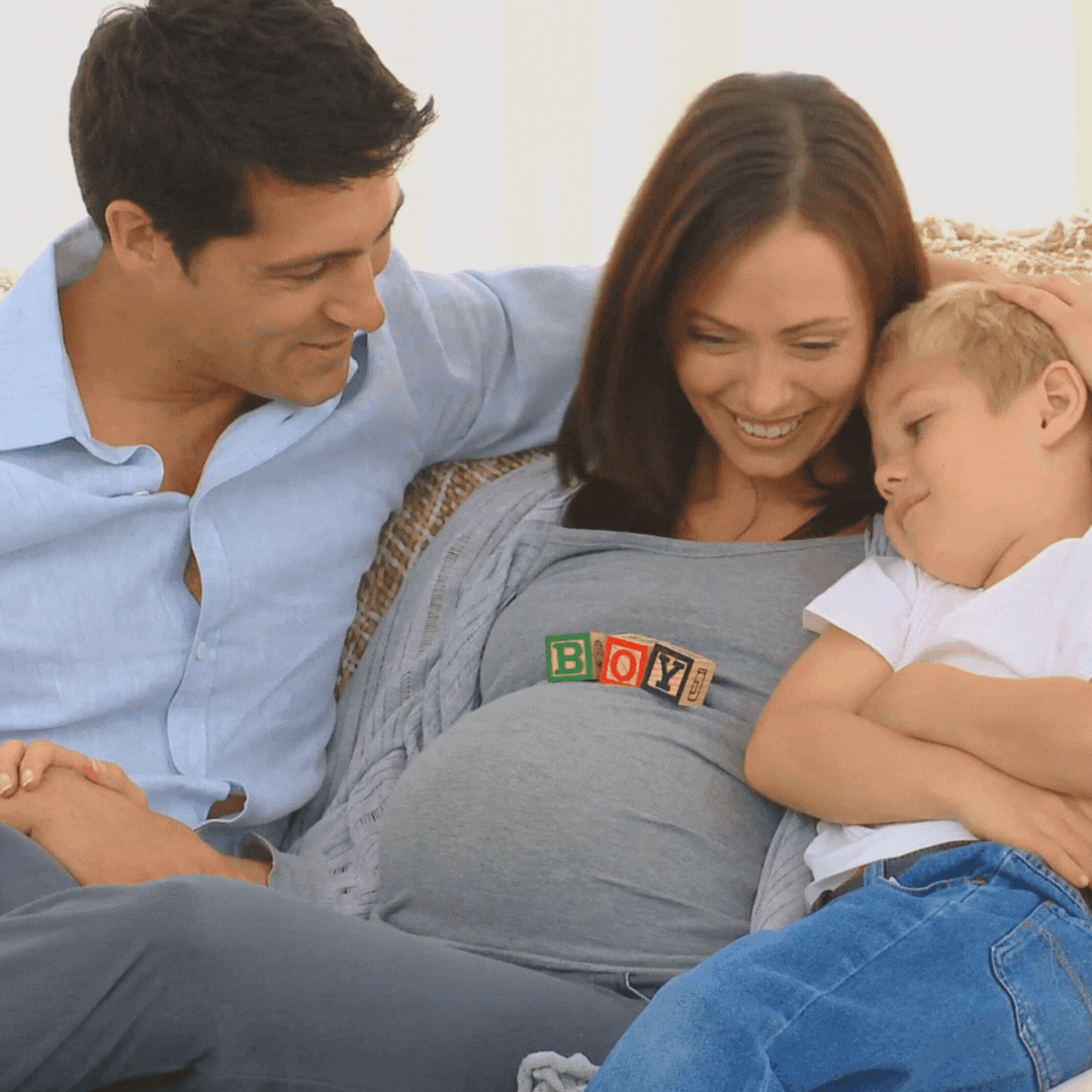 Pregnant sitting on a couch with her husband and toddler, enjoying family time together at home. 