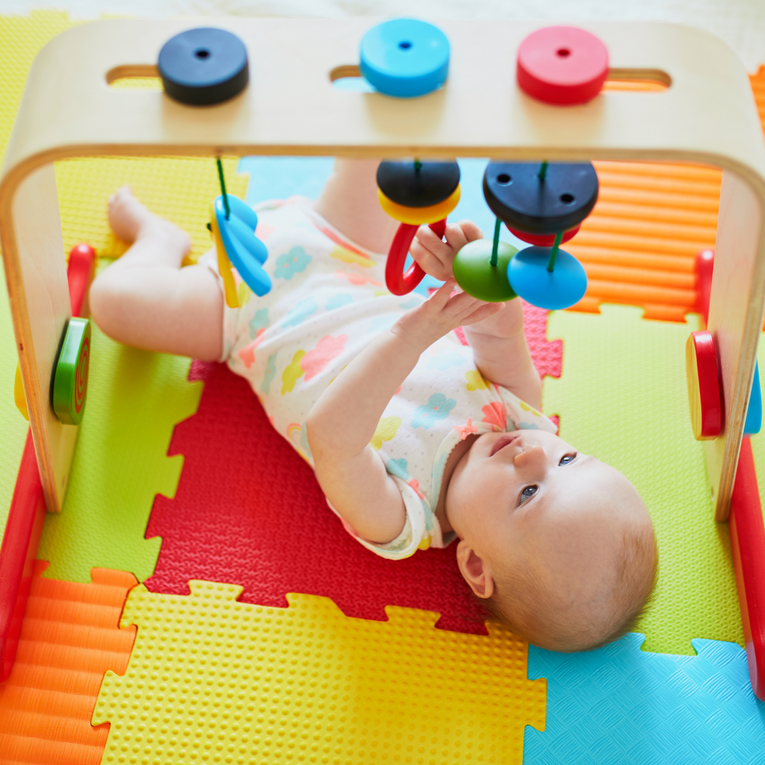 A baby lying in its activity mat playing in hangging toys.