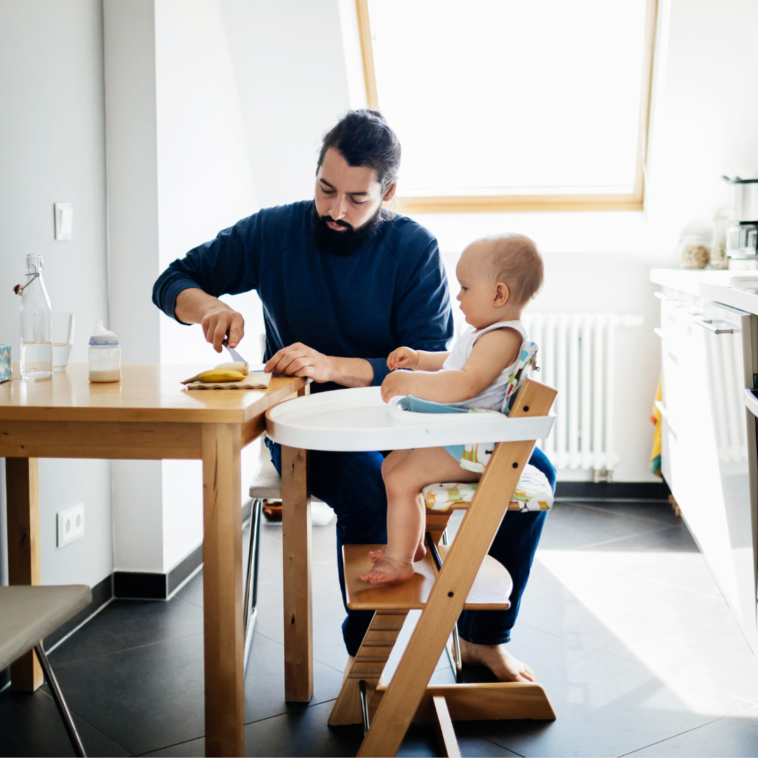 A father eating with his son sitting in a high chair