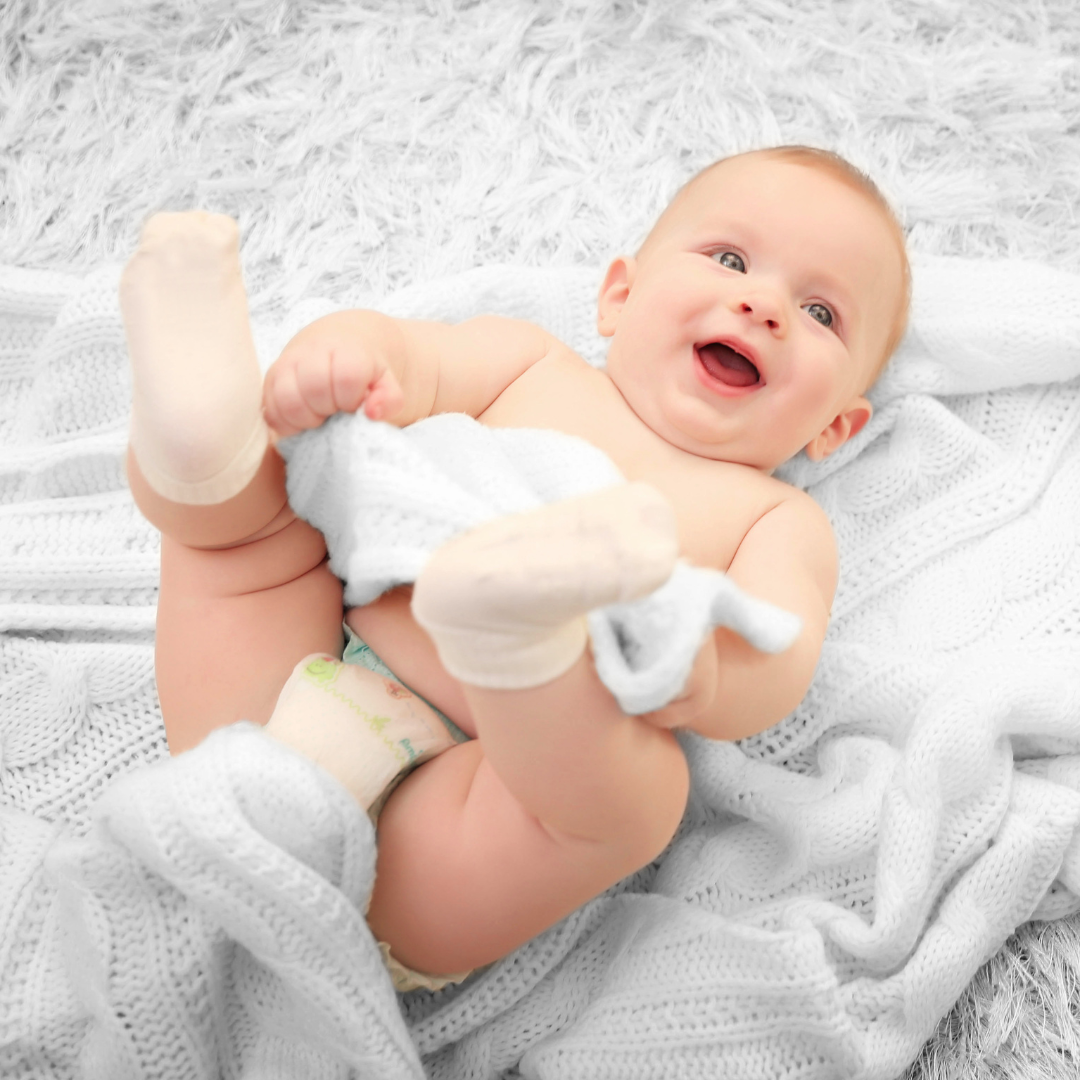 A baby happily plays on its blanket. 