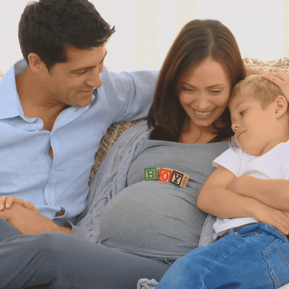 Pregnant sitting on a couch with her husband and toddler, enjoying family time together at home.